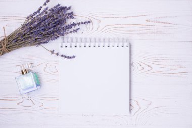 Metnin için temiz bir günlükten bir kompozisyon, bir demet lavanta ve beyazlatılmış ahşap bir masada bir şişe parfüm. Düz yatıyordu.