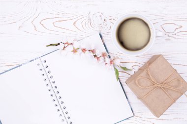 Boş günlükle bahar kompozisyonu, bir fincan kahve, kraft kağıdına sarılı hediye, beyaz ahşap bir masada çiçekli bahar çiçekli badem dalı. Düz yat, boşluğu kopyala