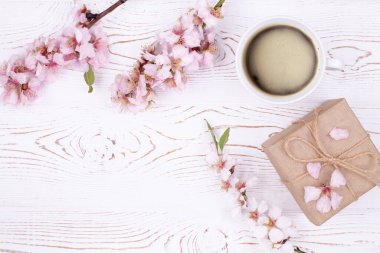 Kahveli bahar kompozisyonu, el işi kağıdına sarılı bir hediye, beyaz ahşap bir masada çiçeklerle açan badem dalları. Düz yat, boşluğu kopyala