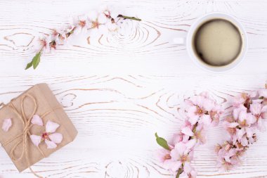 Kahveli bahar kompozisyonu, el işi kağıdına sarılı bir hediye, beyaz ahşap bir masada çiçeklerle açan badem dalları. Düz yat, boşluğu kopyala