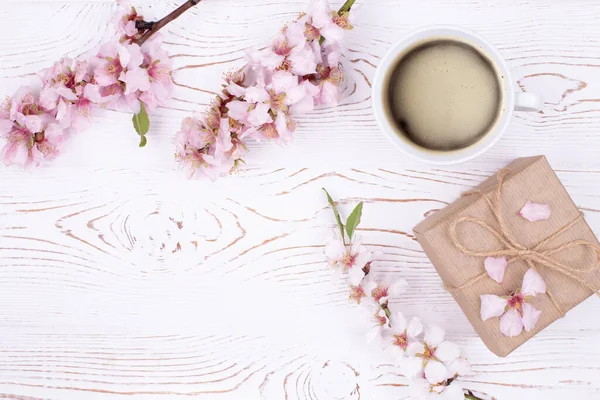 Kahveli bahar kompozisyonu, el işi kağıdına sarılı bir hediye, beyaz ahşap bir masada çiçeklerle açan badem dalları. Düz yat, boşluğu kopyala