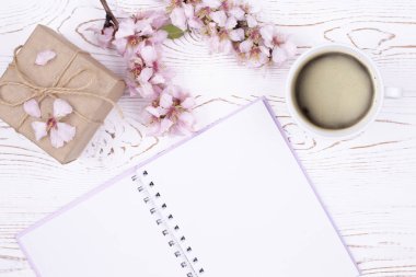 Fikirler, planlar, kahve fincanı, kraft kağıdına sarılı hediye, beyaz ahşap masadaki çiçeklerle açan badem dallı bahar kompozisyonu. Düz yat, boşluğu kopyala.