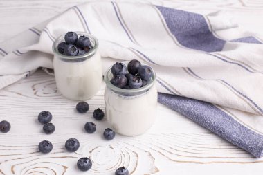 Cam kavanozlarda Yunan yoğurdu ve kırsal beyaz bir masada taze yaban mersini. Cam kavanoza odaklan