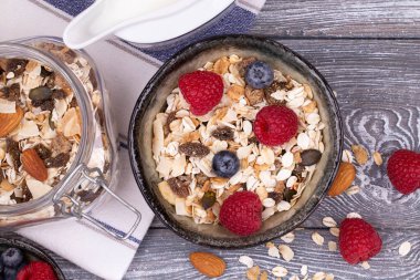 Ev yapımı tahıl gevreği, fındık, ahududu ve yaban mersini, gri beyazlatılmış kırsal masa üzerinde süt, üst manzara, kopyalama alanı. Sağlıklı kahvaltı..