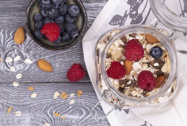 Ev yapımı tahıl gevreği, fındık, ahududu ve yaban mersini, gri beyazlatılmış kır masası, üst manzara, kopyalama alanı. Sağlıklı kahvaltı..