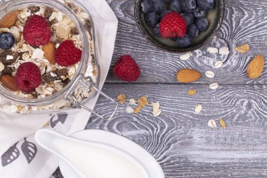 Ev yapımı tahıl gevreği, fındık, ahududu ve yaban mersini, gri beyazlatılmış kırsal masa üzerinde süt, üst manzara, kopyalama alanı. Sağlıklı kahvaltı..