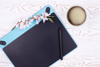 Grafik tableti, grafik kalemi, kahve fincanı ve çiçekli çiçek açan badem dalı olan işyeri manzarası, beyazlatılmış masadaki kopya alanı. Düz stil. Bahar havası