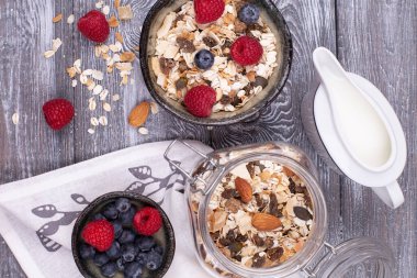 Ev yapımı tahıl gevreği, fındık, ahududu ve yaban mersini, gri beyazlatılmış kır masasında süt, düz konum, fotokopi alanı. Sağlıklı kahvaltı.