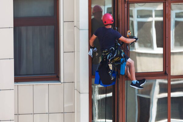 Window washer at work . Man hanging on a rope in helmet