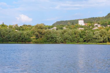 Nehirli yeşil kıyı şeridi. Nehir kenarındaki tepede bir kale 
