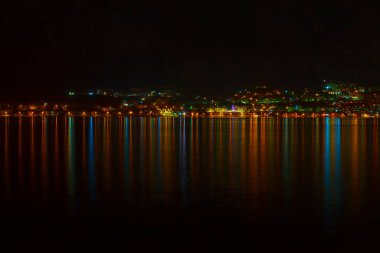 Gece Kotor Körfezi 'ni aydınlattı. Suda yansıması olan sahil kenti ışıkları  