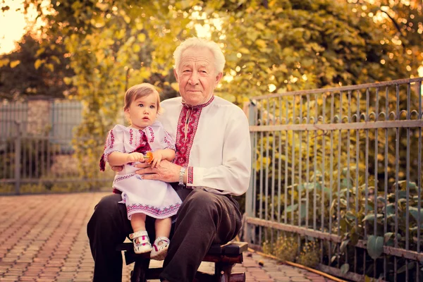 Grandfather with granddaughter in Ukrainian costume at sunset — Stock Photo, Image