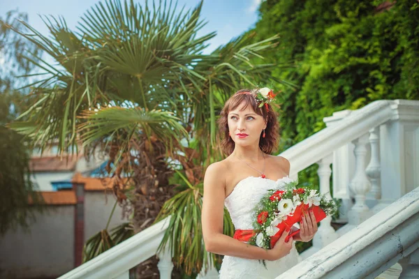 Una bella sposa in natura con un bouquet di rosso — Foto Stock