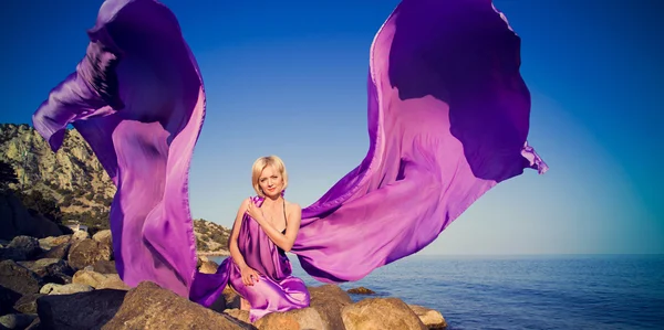 Beautiful girl sitting on a rock near the water — Stock Photo, Image