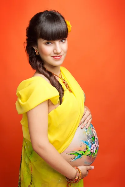 Una chica embarazada con un vestido amarillo sobre fondo naranja —  Fotos de Stock