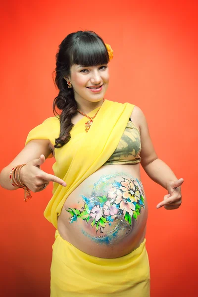 Femme enceinte sur un fond orange montre sur son ventre — Photo