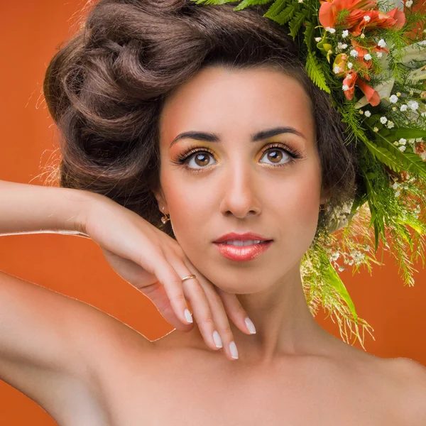 Ein schönes Mädchen mit Blumen auf dem Kopf auf einem orangefarbenen Hintergrund — Stockfoto