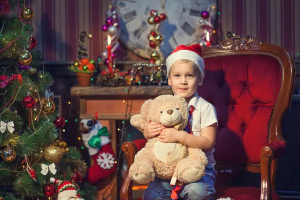 Ein kleiner Junge hält einen Teddybär in der Nähe des Neujahrsbaums Stockfoto