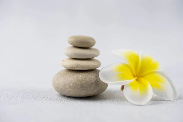 Beyaz zemin üzerinde gri ve beyaz zen çakıl taşı meditasyon taşlarından piramitler ve plumeria tropikal çiçekleri. Uyum kavramı, denge ve meditasyon, spa, masaj, rahatlama