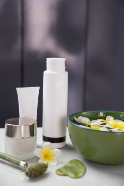 Plumeria çiçekleriyle harika bir spa kompozisyonu. Yüz silindiri ve Guasha masaj aleti. Yüz bakımı, anti-yaş ürünleri ve krem. Çin Gua Sha masaj aletleri.