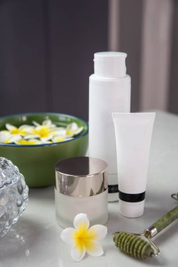 Plumeria çiçekleriyle harika bir spa kompozisyonu. Yüz silindiri ve Guasha masaj aleti. Yüz bakımı, anti-yaş ürünleri ve krem. Çin Gua Sha masaj aletleri.