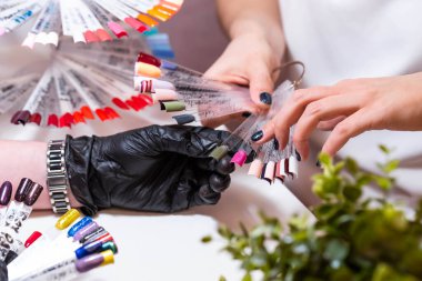 Güzellik salonunda bir müşterisi olan usta manikür ve pedikür dolabında jel rengini seçiyor. Müşteri seçimi için çok renkli oje paletinde farklı oje renkleri var. Tırnak sanatı 