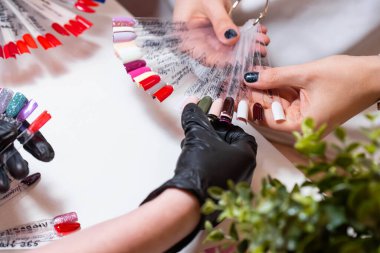 Güzellik salonunda bir müşterisi olan usta manikür ve pedikür dolabında jel rengini seçiyor. Müşteri seçimi için çok renkli oje paletinde farklı oje renkleri var. Tırnak sanatı 