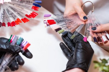 Güzellik salonunda bir müşterisi olan usta manikür ve pedikür dolabında jel rengini seçiyor. Müşteri seçimi için çok renkli oje paletinde farklı oje renkleri var. Tırnak sanatı 