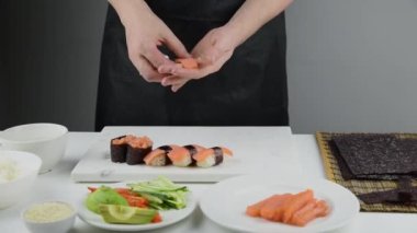 Suşi şefinin ellerini kapatın ve Japon yemeği hazırlayın. Adam restoranda suşi pişiriyor. Geleneksel Asya deniz ürünleri kesim tahtasının üzerinde.