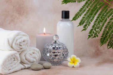 Sağlık merkezindeki masaj masasında spa natürmort bezi. Bej arka planda aromatik mumlarla kıvrılmış sıcak havlu. Aroma terapi seti. Uyum kavramı, denge ve meditasyon, rahatla, güzellik.