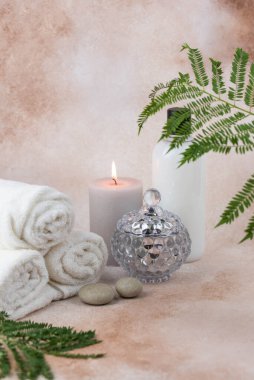 Sağlık merkezindeki masaj masasında spa natürmort bezi. Bej arka planda aromatik mumlarla kıvrılmış sıcak havlu. Aroma terapi seti. Uyum kavramı, denge ve meditasyon, rahatla, güzellik.