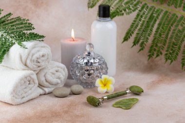 Sağlık merkezindeki masaj masasında spa natürmort bezi. Aromatik mumlarla kıvrılmış sıcak havlu ve bej arka planda yüz silindiri gua sha. Aroma terapi ayarları. 