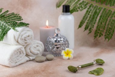 Sağlık merkezindeki masaj masasında spa natürmort bezi. Aromatik mumlarla kıvrılmış sıcak havlu ve bej arka planda yüz silindiri gua sha. Aroma terapi ayarları. 