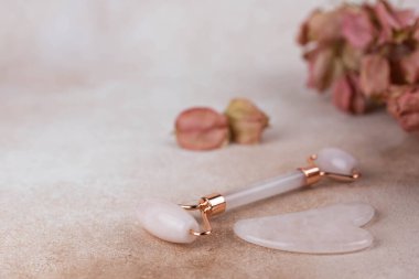 Yüz silindiri ve bej arka planda kuru çiçekli guasha masajı..