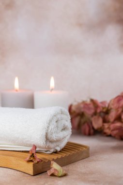 Sağlık merkezindeki masaj masasında spa natürmort bezi. Bej arka planda aromatik mumlarla kıvrılmış sıcak havlu. Aroma terapi seti. Uyum kavramı, denge ve meditasyon, rahatla, güzellik.