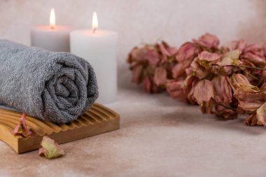 Sağlık merkezindeki masaj masasında spa natürmort bezi. Bej arka planda aromatik mumlarla kıvrılmış sıcak havlu. Aroma terapi seti. Uyum kavramı, denge ve meditasyon, rahatla, güzellik.