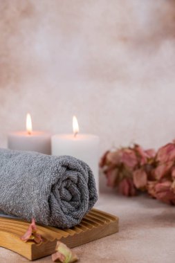 Sağlık merkezindeki masaj masasında spa natürmort bezi. Bej arka planda aromatik mumlarla kıvrılmış sıcak havlu. Aroma terapi seti. Uyum kavramı, denge ve meditasyon, rahatla, güzellik.