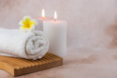 Sağlık merkezindeki masaj masasında spa natürmort bezi. Bej arka planda aromatik mumlarla kıvrılmış sıcak havlu. Aroma terapi seti. Uyum kavramı, denge ve meditasyon, rahatla, güzellik.