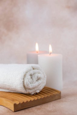 Sağlık merkezindeki masaj masasında spa natürmort bezi. Bej arka planda aromatik mumlarla kıvrılmış sıcak havlu. Aroma terapi seti. Uyum kavramı, denge ve meditasyon, rahatla, güzellik.