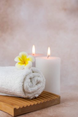Sağlık merkezindeki masaj masasında spa natürmort bezi. Bej arka planda aromatik mumlarla kıvrılmış sıcak havlu. Aroma terapi seti. Uyum kavramı, denge ve meditasyon, rahatla, güzellik.