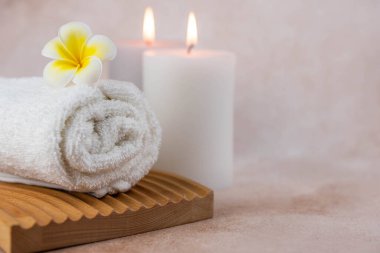 Sağlık merkezindeki masaj masasında spa natürmort bezi. Bej arka planda aromatik mumlarla kıvrılmış sıcak havlu. Aroma terapi seti. Uyum kavramı, denge ve meditasyon, rahatla, güzellik.