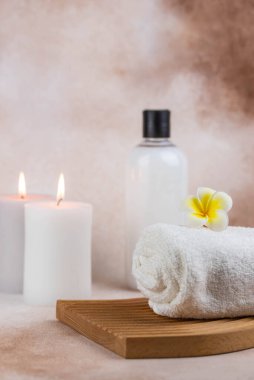 Sağlık merkezindeki masaj masasında spa natürmort bezi. Bej arka planda aromatik mumlarla kıvrılmış sıcak havlu. Aroma terapi seti. Uyum kavramı, denge ve meditasyon, rahatla, güzellik.