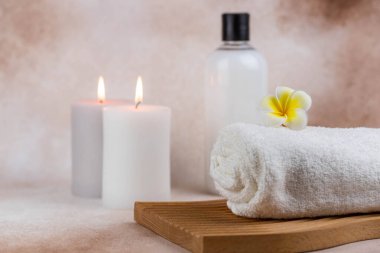 Sağlık merkezindeki masaj masasında spa natürmort bezi. Bej arka planda aromatik mumlarla kıvrılmış sıcak havlu. Aroma terapi seti. Uyum kavramı, denge ve meditasyon, rahatla, güzellik.