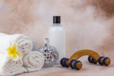 Sağlık merkezindeki masaj masasında spa natürmort bezi. Aromatik mumlarla kıvrılmış sıcak havlu ve bej arka planda ahşap masaj aleti. Aroma terapi ayarları. 