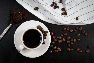 Beyaz bardakla hayat, lezzetli kahve ve kahve çekirdekleri, koyu arka planda.