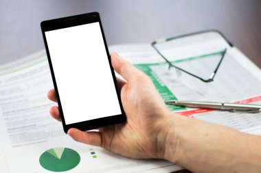 Ofis masasında elinde kağıt, gözlük ve kalemle akıllı telefon tutan bir adamın elini kapat.