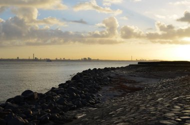 Önünde kaya ve taşlar olan soğuk denizin ve dramatik günbatımının ya da şafak vakti gökyüzünün fotoğrafı.