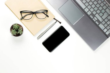 İş yeri yukarıdan dizüstü bilgisayar, not defteri, siyah akıllı telefon, küçük kaktüs, kalem ve gözlüklerle dolu.