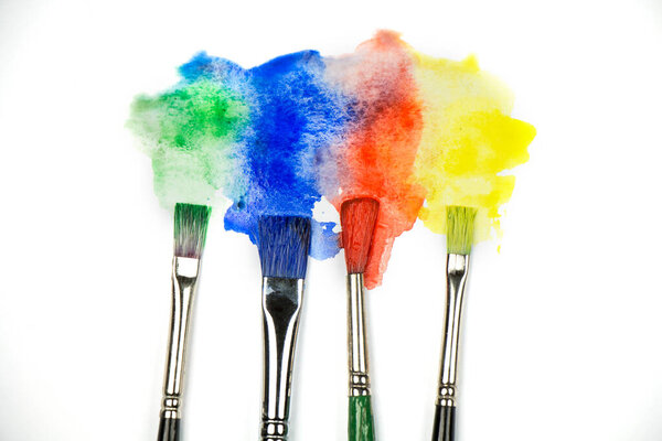 Close up of colorful watercolor stains with paintbrushes on white background