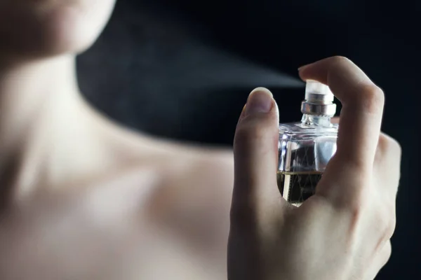 Close up of a woman\'s hand applying perfume with dark background